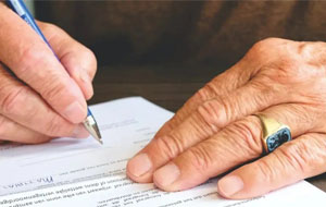 A man's hands resting on a desk and signing a contract