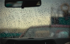 The inside of a windshield facing forwards and water drops falling down