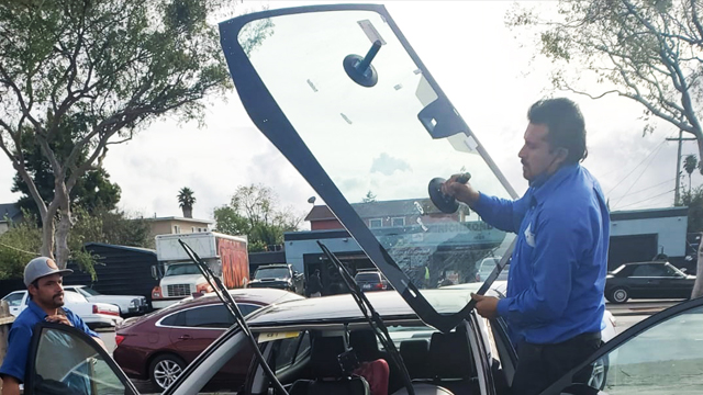 A technician holding a windshield with a tool